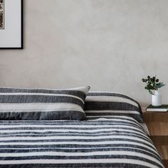 a bed with black and white striped comforter next to a wooden night stand holding a potted plant