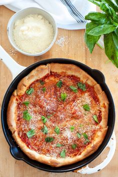 a pizza sitting in a pan on top of a wooden table next to a bowl