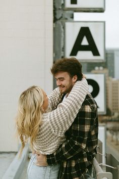 a man and woman embracing each other in front of a sign