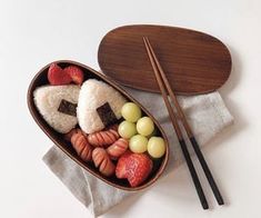 a bento box with chopsticks and fruit in it next to a wooden spoon