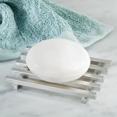 a white soap dish sitting on top of a metal rack next to a blue towel