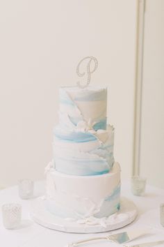 a white and blue wedding cake sitting on top of a table next to silver utensils