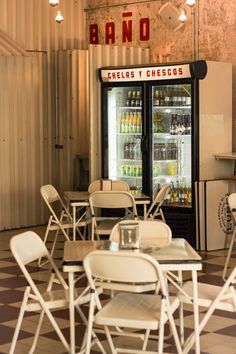 an empty restaurant with tables and chairs in front of a refrigerator filled with sodas