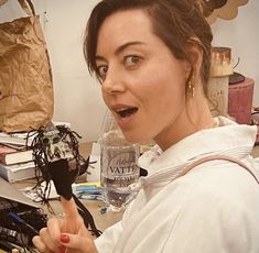 a woman holding a microphone in front of a computer desk with various items on it