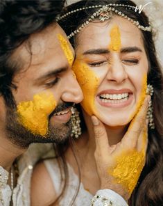 a man and woman with yellow paint on their faces smiling at each other's eyes