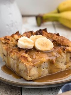 a slice of banana bread pudding on a plate with syrup and bananas in the background