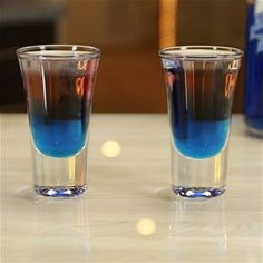 two shot glasses sitting on top of a table next to each other with blue liquid in them