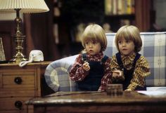 two little boys sitting on a couch with remotes in their hands and looking at the camera