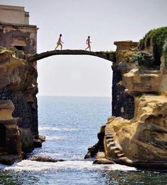 two people are walking on an old bridge over the water