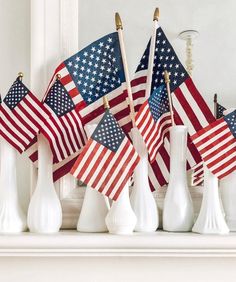 several american flags are placed in white vases on a mantle with candlesticks