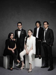 a group of people standing next to each other in front of a gray background with one person wearing a suit and tie