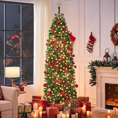 a decorated christmas tree in front of a fireplace with lit candles and stockings on the mantle