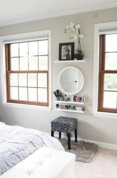 a bedroom with two windows and a white bed in front of the window is an ottoman