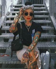 a woman with tattoos sitting on the steps holding her hand up to her head and wearing sunglasses