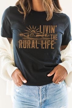 Experience the simple joys of country living with our Livin The Rural Life Western Farm Graphic Tee. Most t shirt colors are 52/48 cotton/poly blend. White and Cream tees are 100% cotton, Ash tees are 99/1 cotton/poly. The classic fit ensures comfortable wear for any rural activity, from farm work to bonfires. Perfect for any country dweller or those who appreciate the rural lifestyle, this tee is a must-have for anyone who loves the simple pleasures of the countryside. Made In: USA Fabric Conte Country Style Cotton Tops For Fall, Country Style Cotton Tops With Letter Print, Country Style Cotton Tops With Relaxed Fit, Country Style Short Sleeve Tops With Letter Print, Country Style Short Sleeve Cotton Tops, Relaxed Fit Country Style Crew Neck T-shirt, Country Style Short Sleeve T-shirt For Spring, Country Style Cotton T-shirt For Summer, Country Style Relaxed Fit Cotton T-shirt