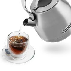 tea being poured into a glass in front of a teapot and saucer on a white background