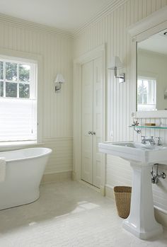 a white bath tub sitting next to a sink in a bathroom under a window with shutters