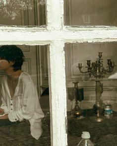 a man and woman kissing in front of a window with the reflection of candles on it