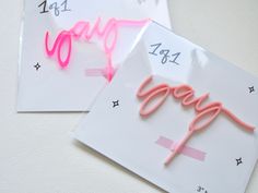 two greeting cards with the word happy written in neon pink on them, one has a pair of scissors next to it