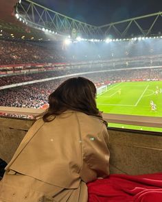 a person sitting on a bench in front of a stadium filled with people watching soccer