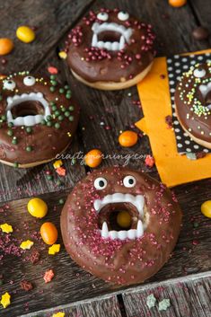 chocolate donuts decorated with sprinkles and candy eyes on a wooden table