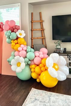 balloons are arranged in the shape of flowers and daisies on a wooden floor next to a television