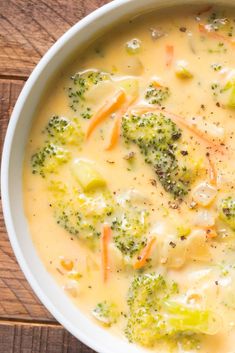 a white bowl filled with broccoli and cheese soup on top of a wooden table