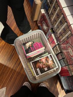 a person standing next to a basket filled with magazines on top of a wooden floor