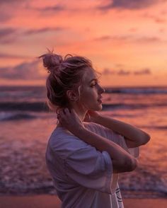 a woman standing on the beach with her arms wrapped around her neck and looking into the distance