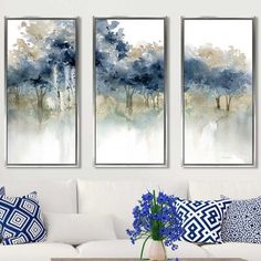 three paintings are hanging on the wall above a white couch with blue and white pillows