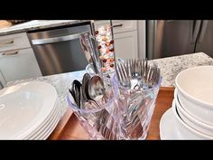 there are many silverware in the glass holder on the kitchen counter with plates and bowls