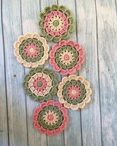 four crocheted flower coasters sitting on top of a wooden table