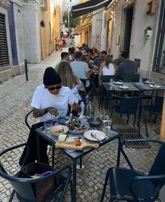 a woman sitting at a table with food in front of her on an alleyway