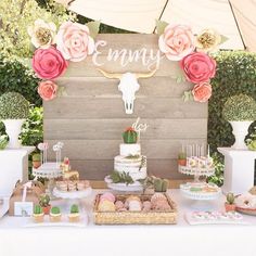 a table topped with lots of desserts covered in pink and white flowers next to a wooden sign