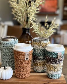 four coffee cups sitting on top of a wooden table next to a vase with white pumpkins