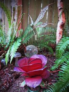 a red flower sitting in the middle of a garden next to green plants and trees