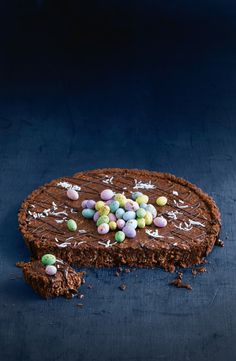 a piece of cake with chocolate frosting and candy eggs on top, sitting on a blue surface