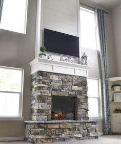 a living room with a stone fireplace and tv above the mantel in front of two windows