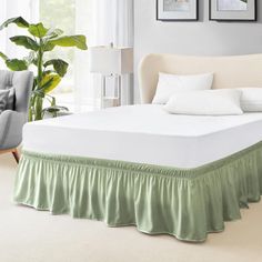 a white bed with green ruffled bedskirt in a living room next to a chair