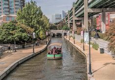 a boat filled with people traveling down a river next to tall buildings on either side