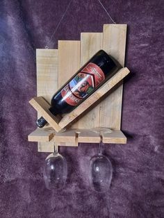 two wine glasses and a bottle hang from a wooden rack on a purple carpeted surface