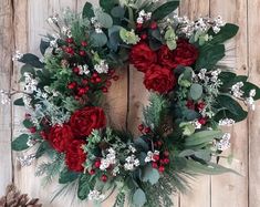 a wreath with red flowers and greenery is hanging on a wooden wall next to a pine cone