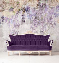 a purple couch sitting in front of a wall with flowers on it's side