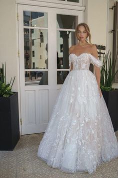 a woman in a white wedding dress standing on the sidewalk with potted plants behind her