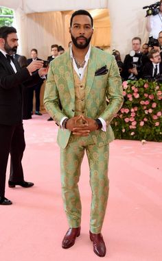 a man in a green suit and tie standing on a pink carpet with people around him