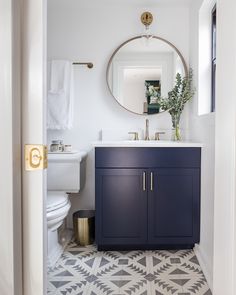 a bathroom with a blue vanity and white toilet next to a mirror on the wall