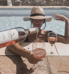 a woman sitting next to a swimming pool pouring wine