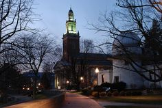 a clock tower lit up at night in front of a building with trees and bushes