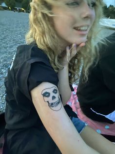 a woman with a skull tattoo on her arm sitting in front of a street corner