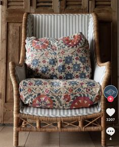 a wicker chair with blue and red floral pillows on it's armrests